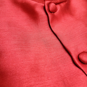 May include: Close-up of a red satin fabric with two buttons. The fabric has a subtle sheen and a smooth texture.