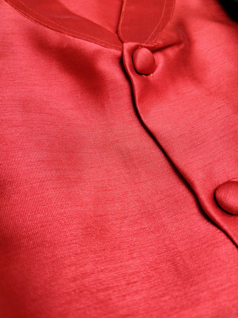 May include: Close-up of a red satin fabric with two buttons. The fabric has a subtle sheen and a smooth texture.