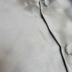 May include: Close-up of a grey, textured fabric with a button fastening. The fabric has a subtle sheen and a smooth, silky feel.