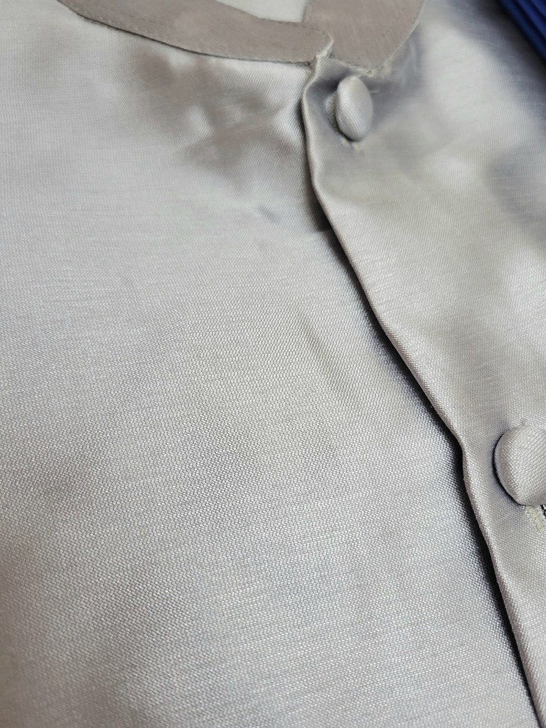 May include: Close-up of a grey, textured fabric with a button fastening. The fabric has a subtle sheen and a smooth, silky feel.