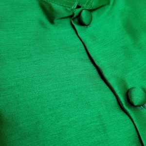May include: Close-up of a green button-up shirt with a mandarin collar. The shirt is made of a smooth, silky fabric.