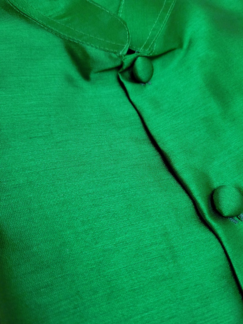 May include: Close-up of a green button-up shirt with a mandarin collar. The shirt is made of a smooth, silky fabric.