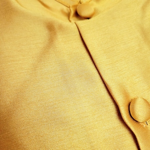 May include: A close-up of a gold fabric with two buttons. The fabric has a subtle texture and a slight sheen.