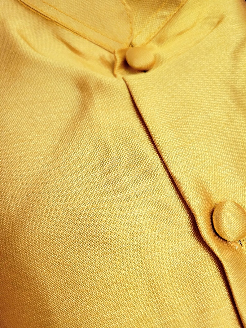 May include: A close-up of a gold fabric with two buttons. The fabric has a subtle texture and a slight sheen.