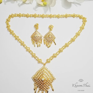 May include: A gold necklace with a large, ornate pendant and matching earrings. The pendant and earrings are decorated with clear rhinestones. The necklace is on a white background. N8