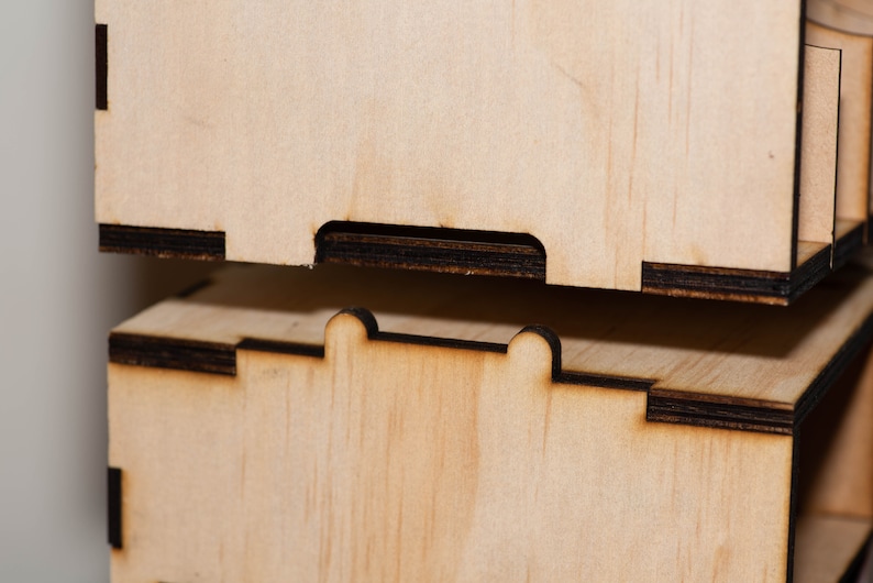 Puede incluir: Dos cajas de madera con bordes negros apiladas una encima de la otra. La caja superior tiene un peque&ntilde;o recorte en el borde delantero. La caja inferior tiene dos peque&ntilde;os recortes en el borde delantero.