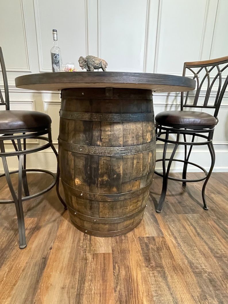 Puede incluir: Una mesa redonda de madera con base de barril, dos sillas de metal negro con asientos de cuero marr&oacute;n y una peque&ntilde;a figura decorativa de b&uacute;falo en la mesa.