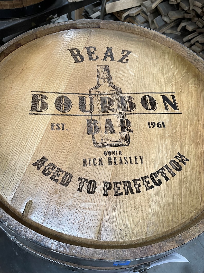 Puede incluir: Un barril de madera con el texto "BEAZ BOURBON BAR EST. 1961 OWNER RICK BEASLEY AGED TO PERFECTION" quemado en la madera.
