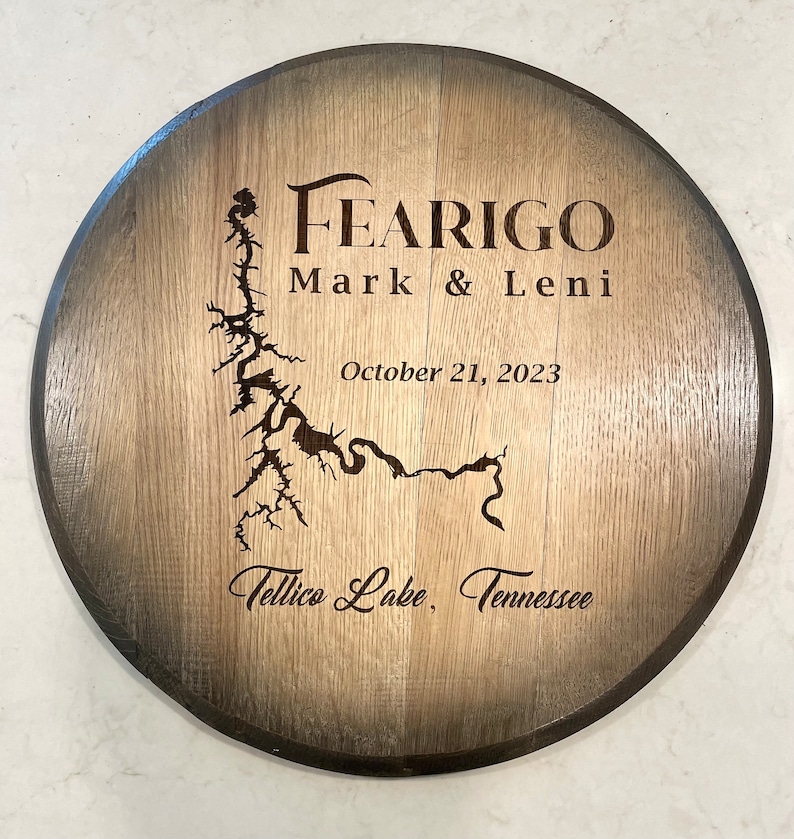 Puede incluir: Un letrero redondo de madera con un borde marr&oacute;n oscuro y un centro marr&oacute;n claro. El letrero est&aacute; grabado con el texto "FEARIGO Mark & Leni October 21, 2023 Tellico Lake, Tennessee" y un mapa de un lago.