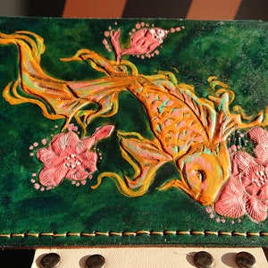May include: A green leather wallet with a detailed embossed design of a gold koi fish and pink flowers.