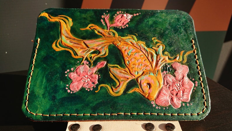 May include: A green leather wallet with a detailed embossed design of a gold koi fish and pink flowers.