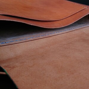 May include: Open view of a brown leather bag with a flap. The interior reveals a lighter brown suede lining and blue stitching. The bag's design suggests a messenger or shoulder bag style.