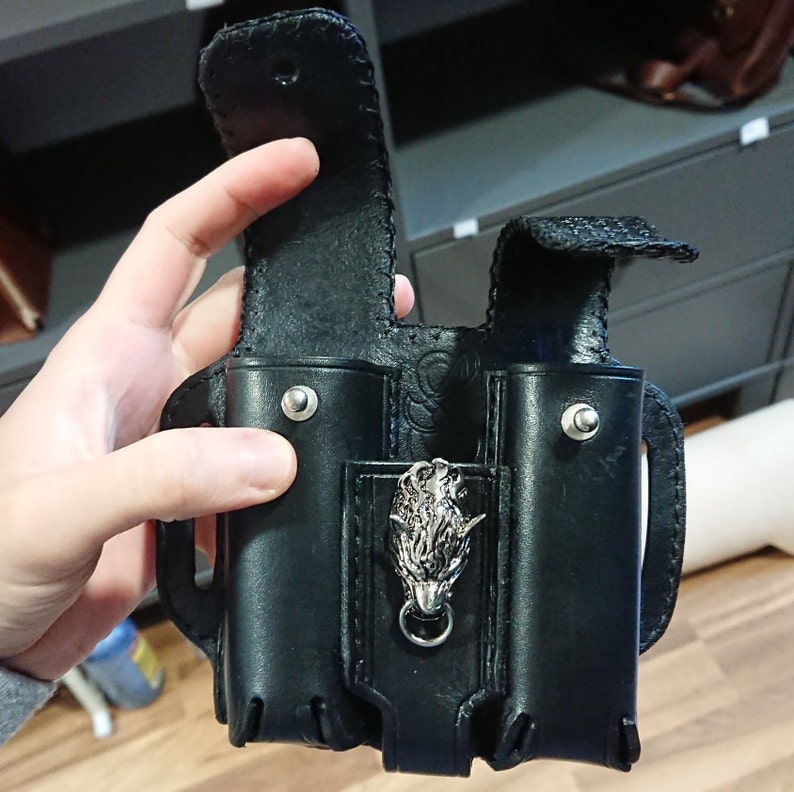 以下が含まれることがあります： 黒い革製のホルスターで、2つのコンパートメントと銀色のオオカミの頭のエンブレムが付いています。 ホルスターはフラップ開閉式で、手で開いています。 革はステッチされ、銀色のリベットが付いています。
