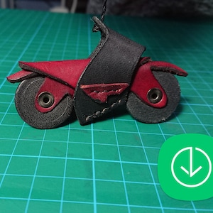 Op de afbeelding: Een kleine, zwarte en rode leren motorfiets sleutelhanger. De motorfiets heeft een rode stoel en zwarte wielen.