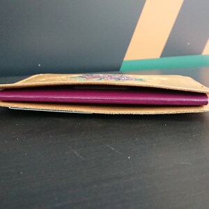 May include: A brown leather passport holder with a floral design. The holder is open and a burgundy passport is inside.