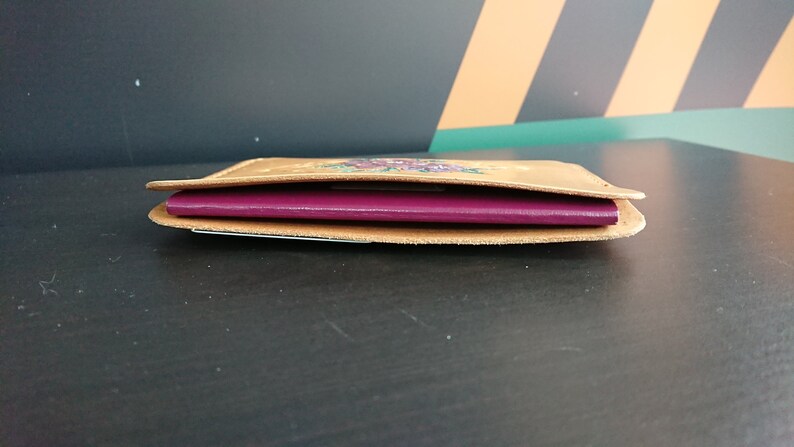 May include: A brown leather passport holder with a floral design. The holder is open and a burgundy passport is inside.