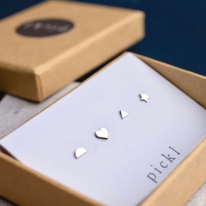 May include: A set of four silver stud earrings in a white box. The earrings are shaped like a half-circle, a heart, a triangle, and a star. The box is labeled "pickl".