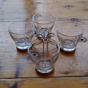 May include: Four clear glass cups with a metal holder. The cups are sitting on a wooden table.