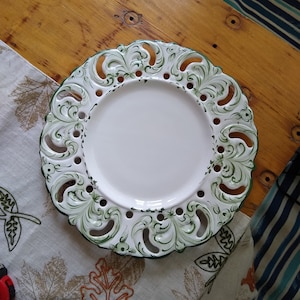 May include: A white ceramic plate with a green and white floral design. The plate has a scalloped edge and is decorated with intricate details.