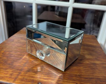 May include: A small mirrored jewelry box with a clear crystal knob. The box has a drawer and a mirrored top.
