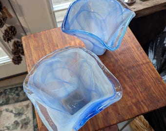 May include: Two blue and white glass vases with a swirled design. The vases are on a wooden table.