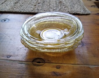 May include: A set of four clear glass bowls with a yellow tint, stacked on top of each other. The bowls have a rippled pattern and are sitting on a wooden surface.