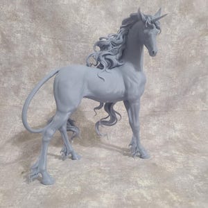 May include: A detailed, gray unicorn sculpture with flowing mane and tail. The mythical creature stands gracefully, showcasing intricate details of its form, including a spiraled horn and delicate hooves. The sculpture is set against a textured, neutral background.