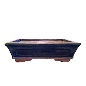 Op de afbeelding: Een rechthoekige keramische bonsaipot met een diep marineblauwe geglazuurde buitenkant en een gladde afwerking. De pot heeft een brede, uitlopende rand, een verzonken paneelontwerp aan de zijkanten en rust op vier kleine, stevige voetjes.