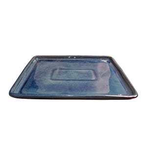 May include: A rectangular ceramic tray with a glossy, blue glaze. The tray has a slightly raised, rectangular indentation in the centre. The edges are slightly raised and the corners are rounded. The tray is suitable for serving food or displaying decorative items.
