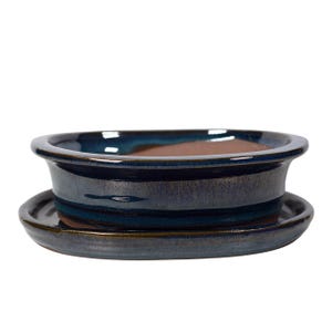Könnte beinhalten: Ein blauer und brauner glasierter Keramik-Bonsai-Topf mit einer passenden Untertasse. Der Topf ist oval geformt und hat einen leicht erhöhten Rand.