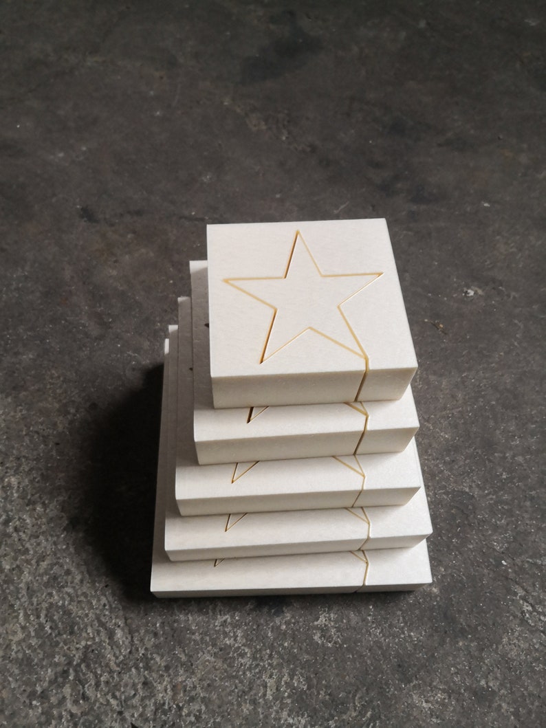 May include: A stack of six white square tiles with a gold star cutout in the center of each tile.