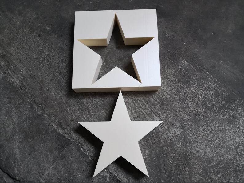 May include: Two white wooden stars, one with a cutout star shape. The larger star is on top of the smaller star.