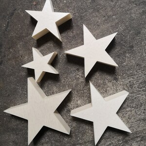May include: Five white wooden stars of varying sizes, arranged in a cluster on a gray textured surface.