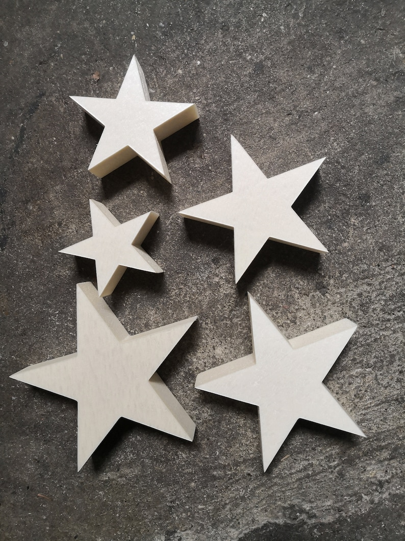 May include: Five white wooden stars of varying sizes, arranged in a cluster on a gray textured surface.