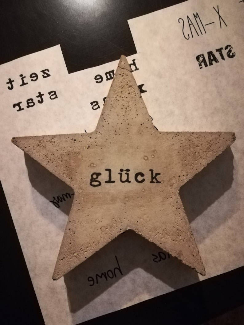 May include: A beige concrete star with the word "gl&uuml;ck" printed in black lettering.