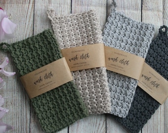 May include: Four handmade washcloths in different colors: green, beige, gray, and charcoal. Each washcloth has a brown paper tag that says "Handmade Wash Cloth 100% Cotton".