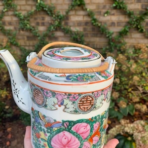 May include: White porcelain teapot with a bamboo handle and a floral design. The teapot features pink and green flowers, and the Chinese character for "happiness" is repeated on the side.