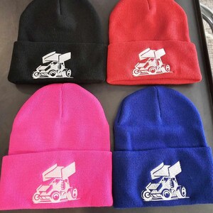 May include: Four knit beanies in black, red, pink, and blue with a white graphic of a race car on each.