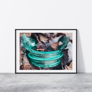May include: A close-up of a broken teal glass jar lid lying on a bed of brown leaves.