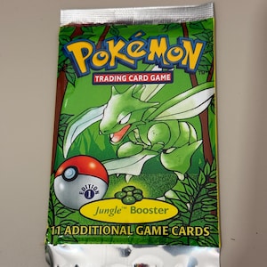 May include: A sealed Pokémon Trading Card Game booster pack. The pack features a green background with a Scyther illustration and the Pokémon logo. Text includes "Jungle Booster" and "11 Additional Game Cards."