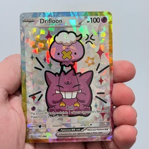 May include: A holographic Drifloon Pokémon card with a purple and white cartoon character. The card has the text "Drifloon" and "HP 100". The card also has the text "Pull" and "Pokémon ex rule".