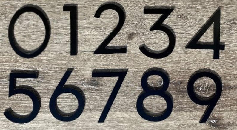 May include: Black metal house numbers 0 through 9 on a wood background.