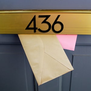 May include: A gold mailbox with the number 436 on it. There are two envelopes sticking out of the mailbox, one is pink and the other is brown.