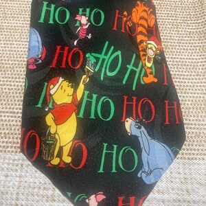 May include: Black necktie featuring Winnie the Pooh characters in Christmas attire. The tie has the words "HO HO HO" in red and green. Winnie the Pooh, Piglet, Tigger, and Eeyore are depicted on the tie.