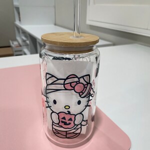 May include: A clear glass tumbler with a bamboo lid and a Hello Kitty Halloween design. The design features Hello Kitty dressed as a mummy holding a jack-o-lantern. The tumbler has a clear plastic straw.