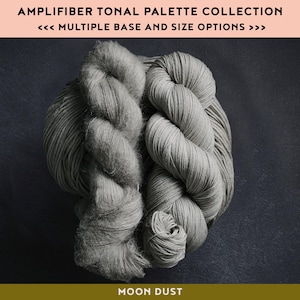 May include: Two skeins of gray yarn are displayed against a dark background. The text "AMPLIFIBER TONAL PALETTE COLLECTION" and "MOON DUST" are visible. The yarn is thick and appears soft, ideal for knitting or crocheting projects.