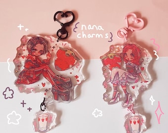 May include: Two acrylic charms featuring anime-style characters, strawberries, and drink illustrations. One charm has a black heart-shaped clasp, the other a pink heart-shaped clasp. The text "nana charms" is visible.