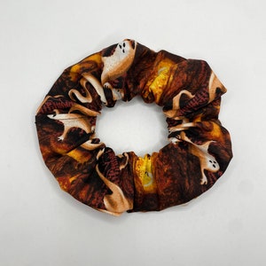 Op de afbeelding: Een bruine en oranje stoffen scrunchie met een wit spookpatroon.