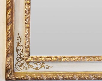 May include: A large, ornate gold mirror with a white frame and intricate gold leaf details. The frame has a raised, textured design and features a decorative pattern in the corners.