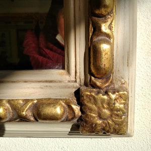 May include: A close-up of a white and gold ornate picture frame. The frame has a decorative design with gold accents and a white background.
